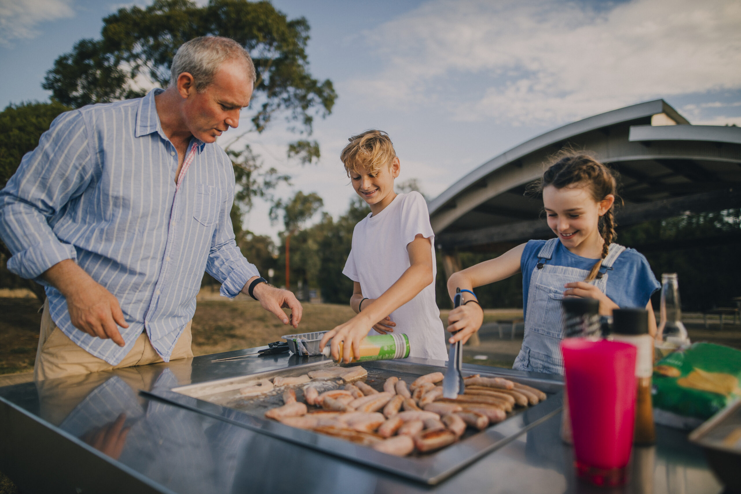 Family cooking sausages on a BBQ in the park