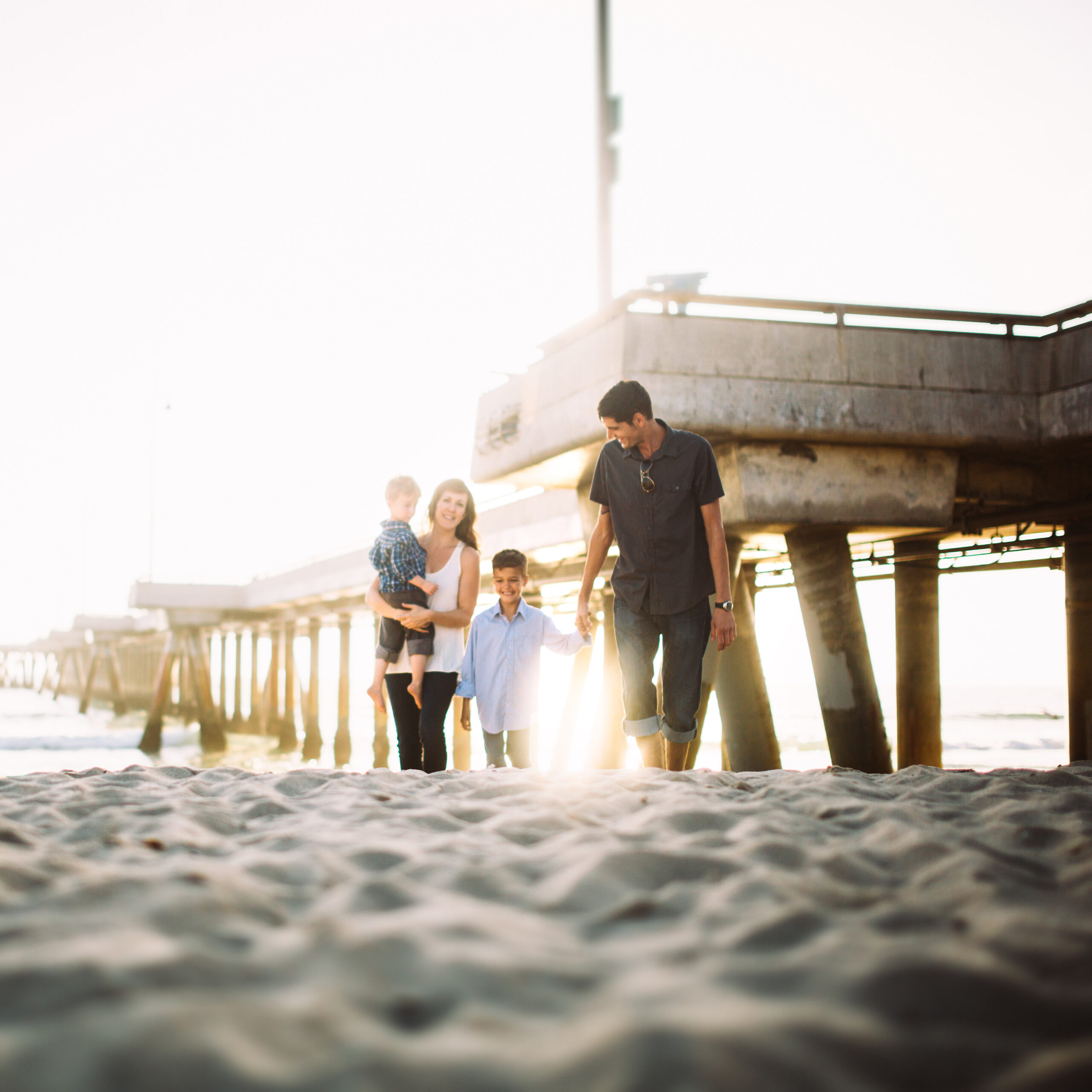 A beautiful young family hold hands and walk up the sands of Venice beach