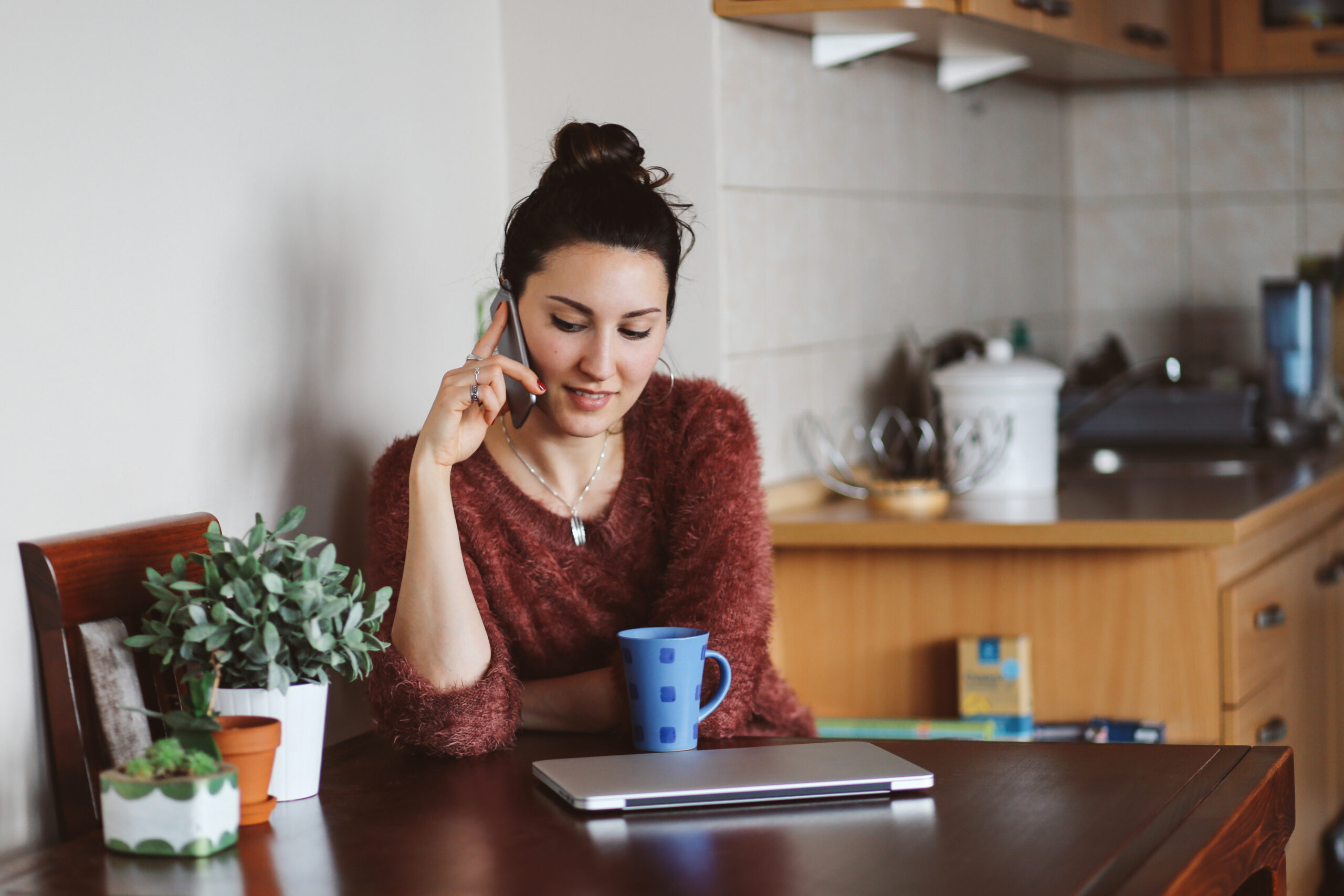 Vintage toned portrait of a young woman, wearing casual clothes, sitting at the table in her living room or kitchen, relaxing, talking on the cellphone